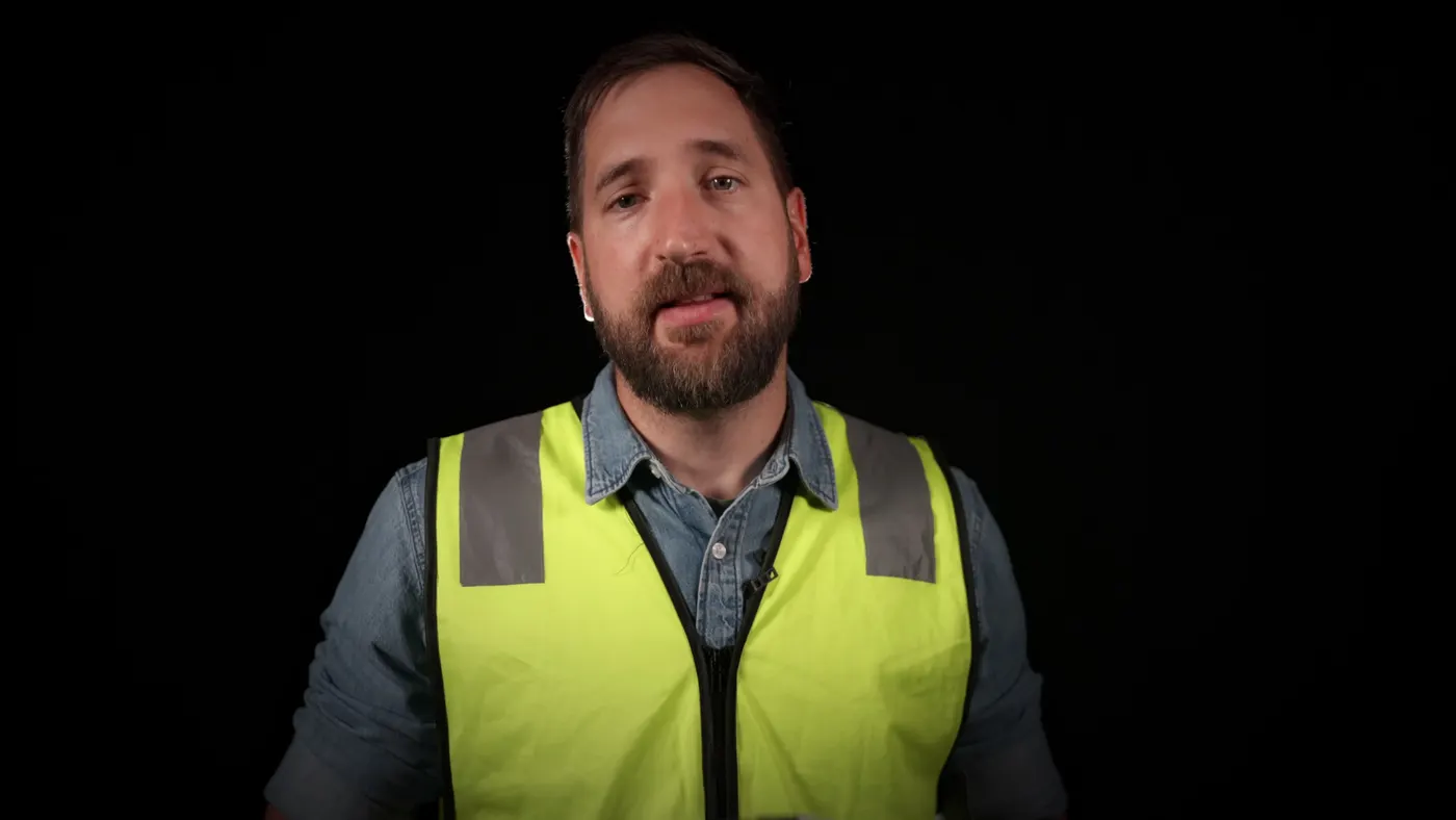 Fagperson i refleksvest snakker til kamera foran svart bakgrunn